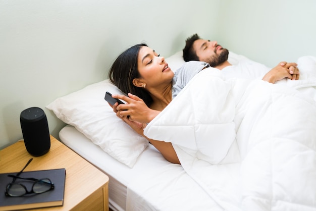 Kostenloses Foto fremdgehende freundin schaut nach ihrem schlafenden freund, während sie einem anderen partner eine sms schreibt, während sie im bett liegt