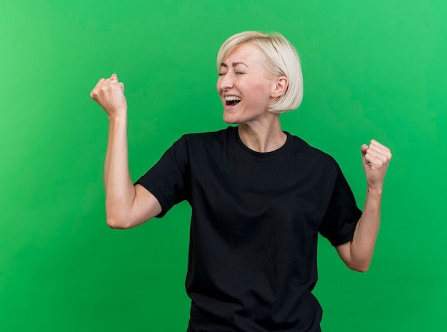 Freudige blonde slawische Frau mittleren Alters, die ja Geste mit geschlossenen Augen tut, lokalisiert auf grünem Hintergrund
