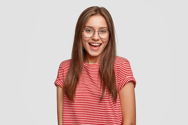 Freudige dunkelhaarige Frau mit zahnigem angenehmem Lächeln, trägt runde transparente Brille, gestreiftes T-Shirt
