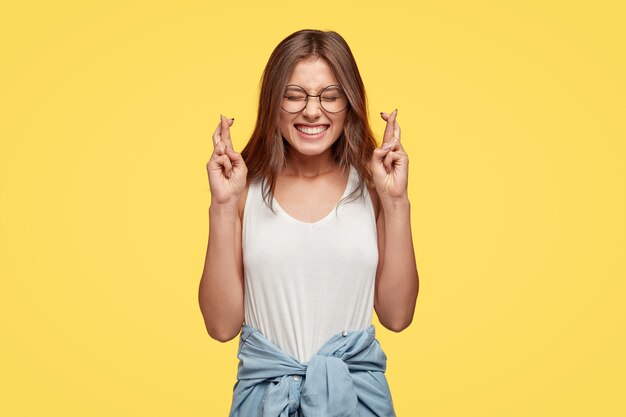 Freudige junge Brünette mit Brille, die gegen die gelbe Wand aufwirft