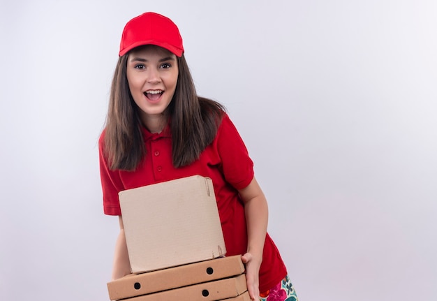 Freudige junge Lieferfrau, die rotes T-Shirt in der roten Kappe trägt, die eine Box und eine Pizzaschachtel auf isolierter weißer Wand hält