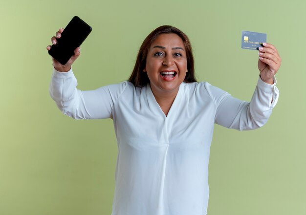freudige lässige kaukasische Frau mittleren Alters, die Telefon mit Kreditkarte anhebt