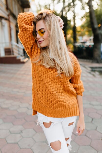 Freudige schlanke Frau in der schönen Strickjacke, die Freizeit im Freien genießt und lächelt