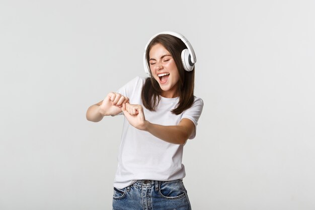 Freudige schöne junge Frau tanzt und genießt Musik in drahtlosen Kopfhörern.