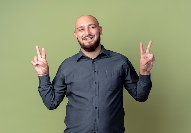 Freudiger junger kahler Callcenter-Mann, der Friedenszeichen lokalisiert auf olivgrün tut