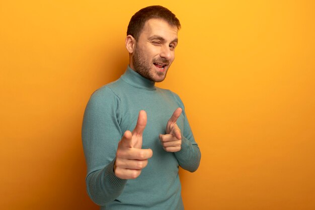 Freudiger junger kaukasischer Mann, der Kamera betrachtet, die zwinkert, dass Sie Geste lokalisiert auf orange Hintergrund mit Kopienraum tun