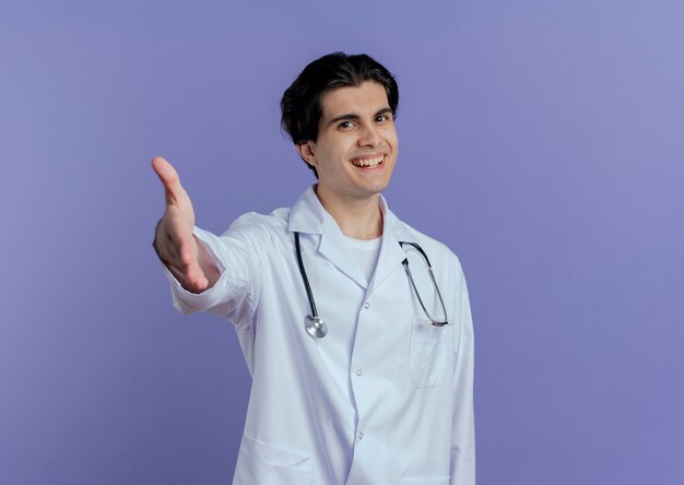 Freudiger junger männlicher Arzt, der medizinische Robe und Stethoskop trägt, die Grußgeste lokalisiert tut