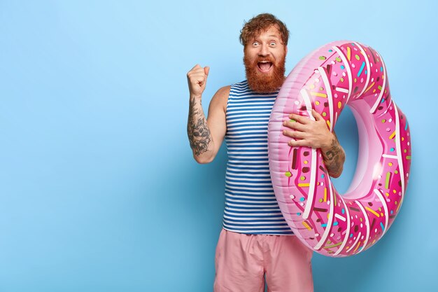 Freudiger rothaariger Mann, der mit schwimmendem Donutpool aufwirft