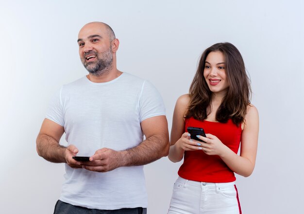 Freudiges erwachsenes Paar, das beide Handys hält und zur Seite schaut