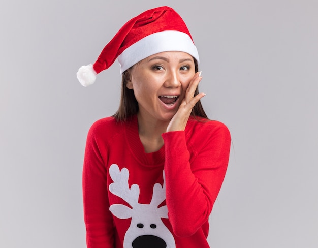 Kostenloses Foto freudiges junges asiatisches mädchen, das weihnachtsmütze mit pullover trägt, der jemanden lokalisiert auf weißem hintergrund nennt