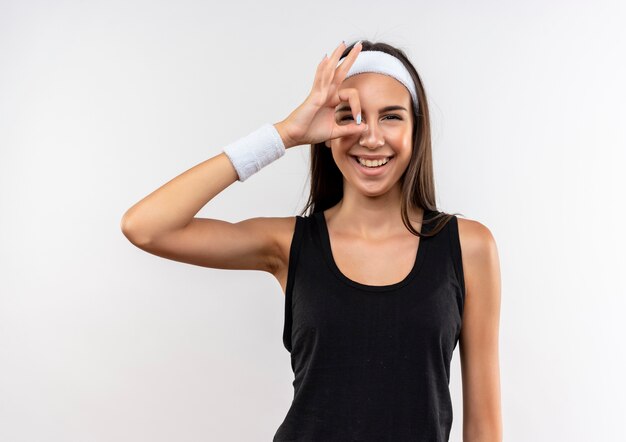 Freudiges junges hübsches sportliches Mädchen, das Stirnband und Armband trägt und Blickgeste auf Weißraum tut