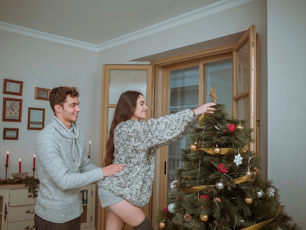 Freund, der die Freundin verziert Weihnachtsbaum mit Stern hält