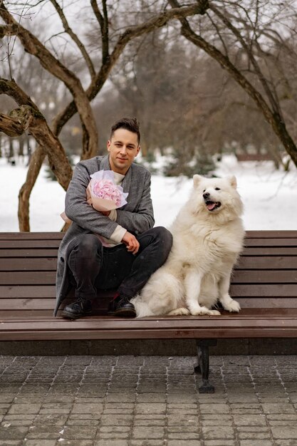 Freund mit einem Strauß rosafarbener Blumenhortensie wartet auf seine Freundin und geht spazieren und spielt mit einem Hund. im Freien, wenn Schnee fällt. Valentinstag-Konzept, Hochzeitsvorschlag. Mangos