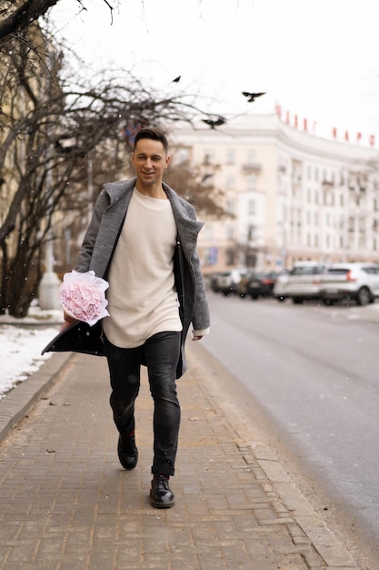 Freund mit einem Strauß rosafarbener Blumenhortensie wartet draußen auf seine Freundin, während Schnee fällt. Valentinstag-Konzept, Hochzeitsvorschlag. Mann geht auf ein Date.