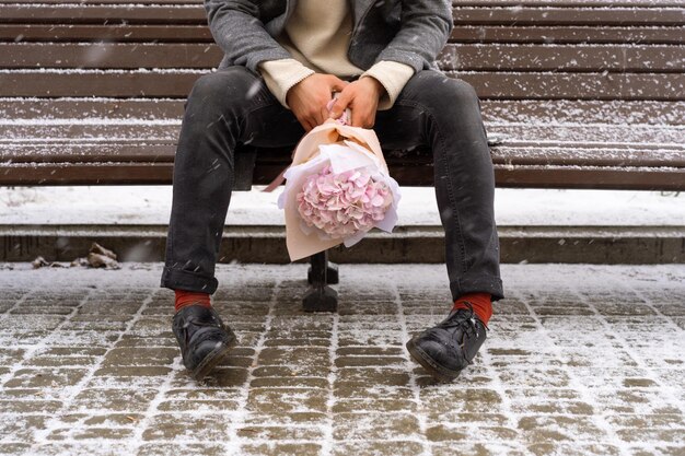 Freund mit einem Strauß rosafarbener Blumenhortensie wartet draußen auf seine Freundin, während Schnee fällt. Valentinstag-Konzept, Hochzeitsvorschlag. Mann geht auf ein Date.