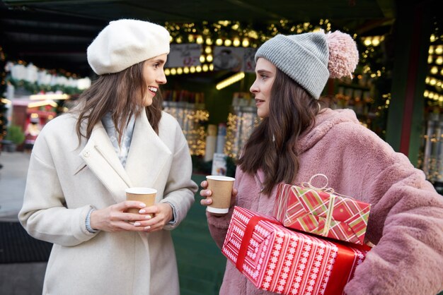 Freunde auf dem Weihnachtsmarkt tragen Geschenke und trinken Glühwein