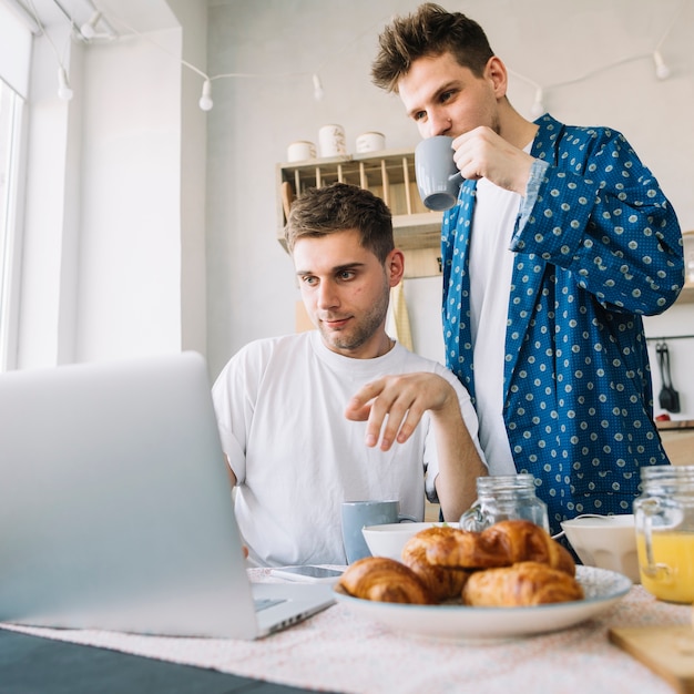 Freunde, die den Kaffee schaut etwas auf Laptop über Tabelle mit geschmackvollem Lebensmittel trinken