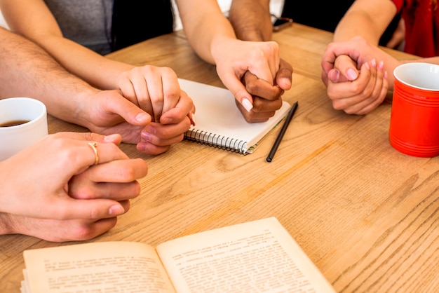 Freunde, die Hände nahe Briefpapier und Kaffeetassen über hölzernem Schreibtisch halten