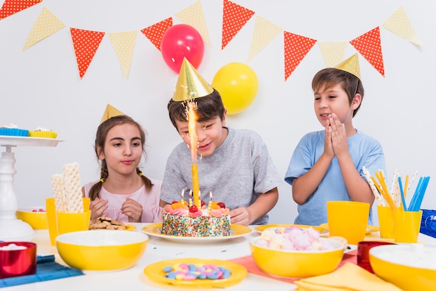 Freunde, die während Junge zu Hause schneiden seinen Geburtstagskuchen klatschen