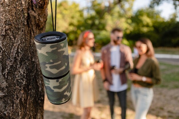 Freunde, die zusammen Spaß im Park haben und lächeln, während sie Musik über den drahtlosen Lautsprecher im Vordergrund hören