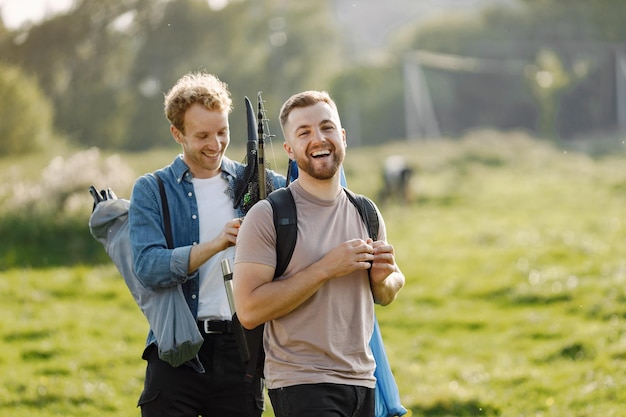 Freunde ist zum Angeln bereit. Der Mann, der eine Angelausrüstung und anderes hält, hilft ihm. Ein Mann trägt ein rosafarbenes T-Shirt und ein anderes blaues Hemd