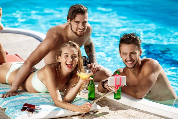 Freunde lächeln, machen Selfie, trinken Cocktails, entspannen in der Nähe von Schwimmbad