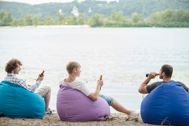 Freunde mit dem Bier, das nahe Wasser sich entspannt