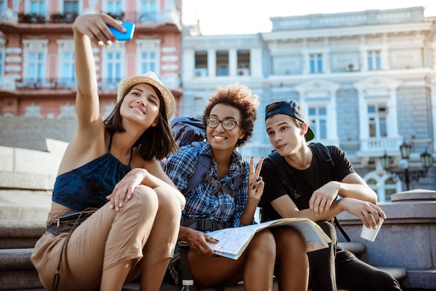 Freunde Reisende mit Rucksäcken lächelnd, Selfie machen, in Sichtweite sitzen.