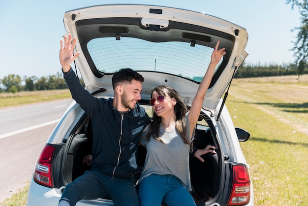 Freunde sitzen auf Autokofferraum machen Friedenszeichen