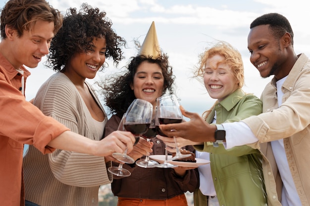 Freunde stoßen mit Gläsern Wein an und essen Kuchen während einer Party im Freien