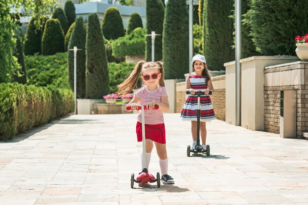 Freundinnen am sonnigen Tag. Kinder im Vorschulalter fahren Roller im Freien.