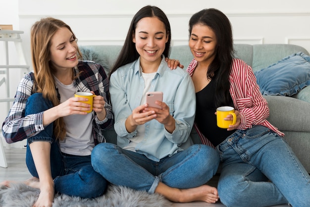 Freundinnen, die auf dem Boden betrachtet Smartphone sitzen