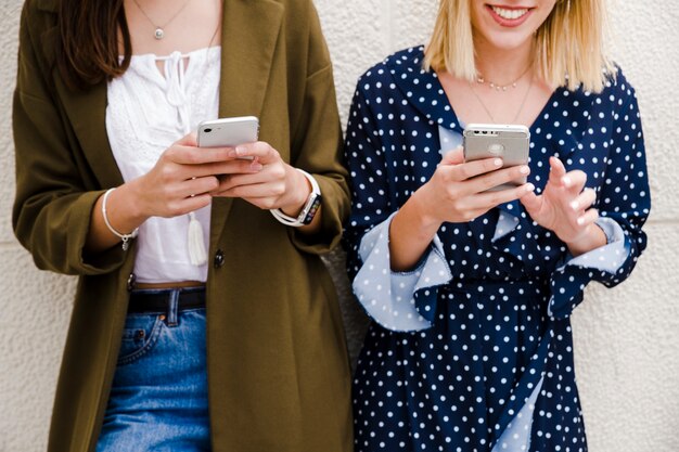 Freundinnen, die auf Wand unter Verwendung des Smartphone sich lehnen