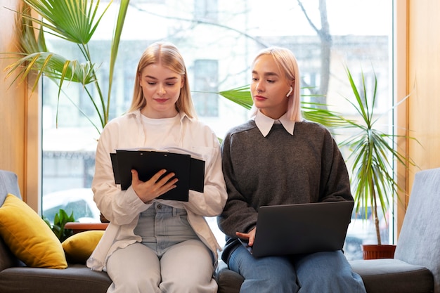 Freundinnen lernen in einer Bibliothek, während sie einen Laptop und ein Notebook benutzen