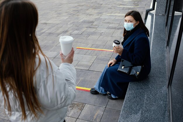 Freundinnen treffen sich beim Kaffee, während sie Masken tragen