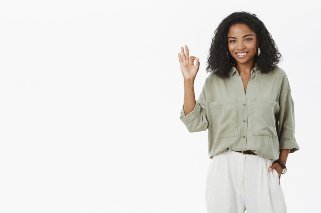 Freundlich aussehende freudige und selbstbewusste Afroamerikanerin mit lockiger Frisur, die ok zeigt