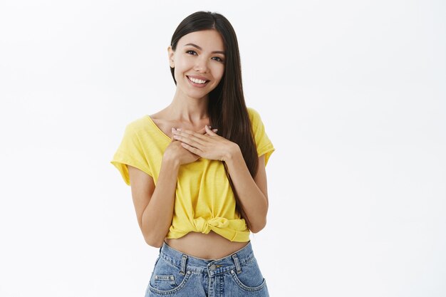 Freundlich aussehende stilvolle erfreute Frau im trendigen gelben T-Shirt und in den Jeansshorts, die Palmen zusammen auf Brust halten