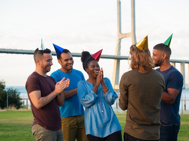 Freundliche junge Leute, die Überraschung für ihren Freund machen. Gute Freunde, die Geschenk für glückliche junge Frau geben. Konzept der Geburtstagsüberraschung