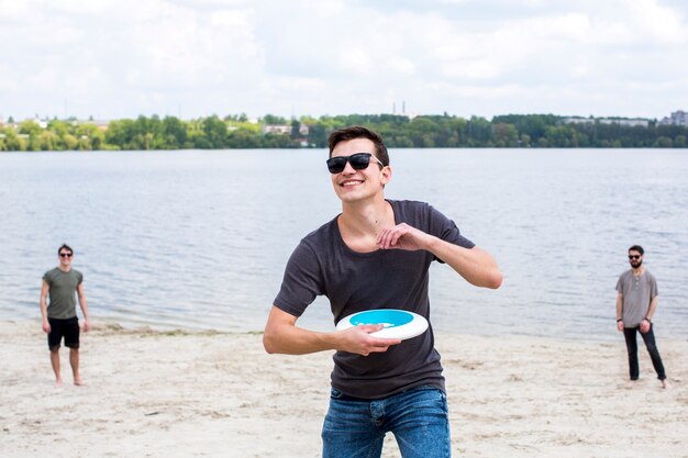 Freundliche männliche Freunde, die Frisbee auf Strand spielen