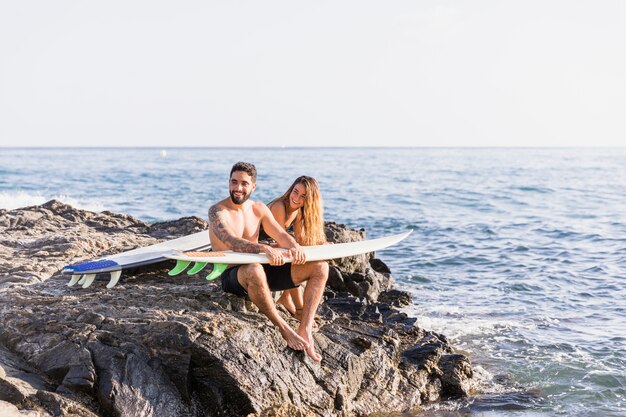 Freundliche Paare mit Surfbrettern auf felsigem Ufer