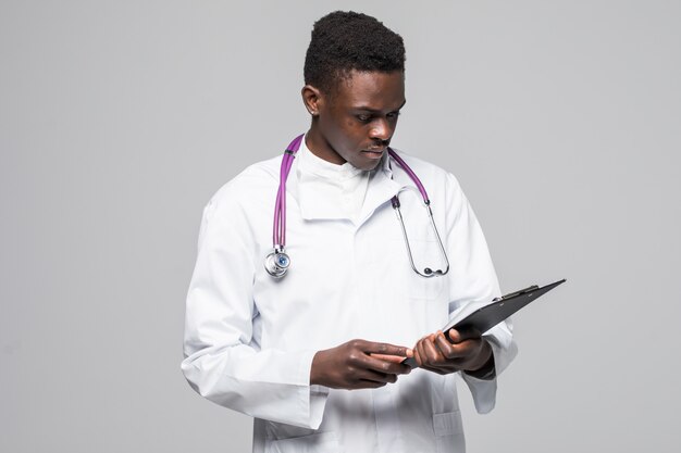 Freundlicher afroamerikanischer Arzt, der eine Zwischenablage hält und die Kamera auf grauem Hintergrund lokalisiert