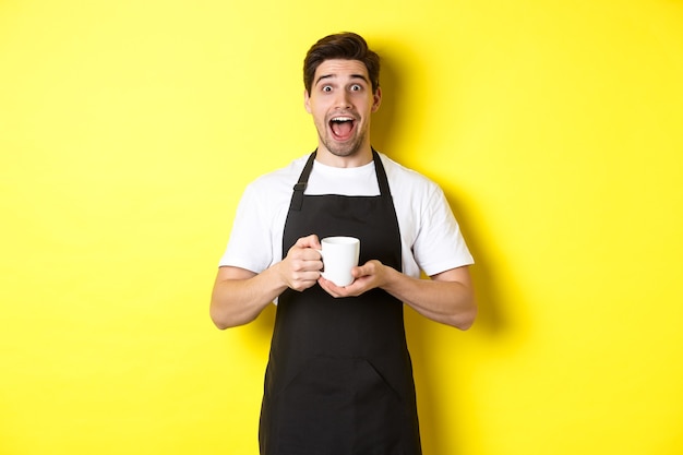 Freundlicher Café-Kellner, der mit erhobenen Händen steht, Platz für Ihr Schild oder Logo, auf gelbem Hintergrund steht.