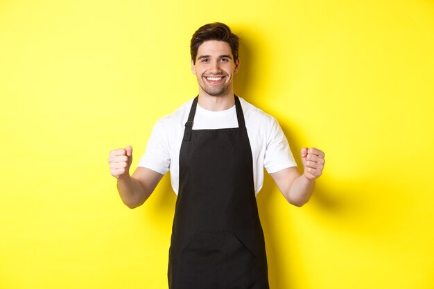 Freundlicher Coffeeshop-Kellner, der mit erhobenen Händen steht, Platz für Ihr Zeichen oder Logo, stehend über gelbem Hintergrund.