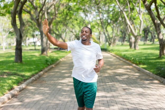 Freundlicher sportlicher schwarzer Kerl, der im Stadtpark rüttelt und vertraute Sportler grüßt.