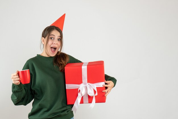 freute sich Mädchen mit Partykappe, die ihr Weihnachtsgeschenk und eine Tasse Tee auf Weiß hält