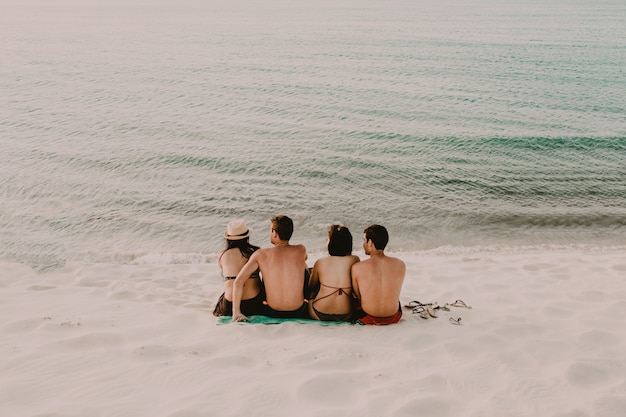 Kostenloses Foto friedlicher strand mit zwei frauen und zwei männern, die nahe dem wasser sitzen