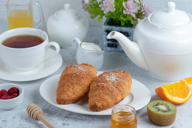 Frisch gebackene Croissants mit einer Tasse Tee und süßen Früchten.