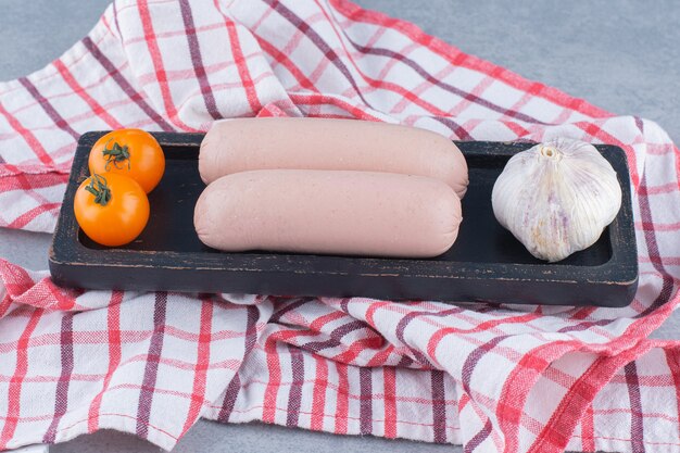 Frisch gekochte Wurst, Knoblauch und Kirschtomate auf schwarzem Holzbrett.