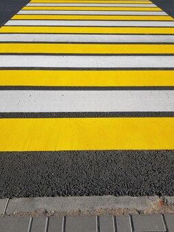 Frisch gestrichener fußgängerüberweg mit gelben und weißen markierungen auf asphalt, vertikales foto, sonnenlicht.