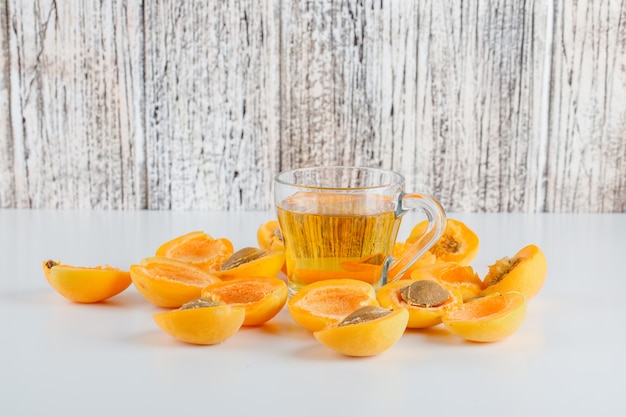 Frische aprikosen mit teeseitenansicht auf weißem und holztisch